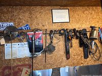 Wide view of various tools hanging on wooden wall including files, planers, and chains, along with safety documents and license plates.