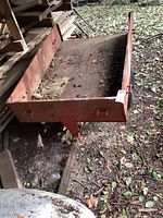 Front perspective view of the wooden two-wheeled trailer showing the trailer bed with red painted wood and some wear.