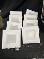 Set of eight square white retrofit recessed can lights with wiring and clips, arranged side by side.