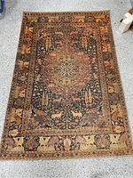 Top-down image showing the full 5 x 7 woven rug with brown, rust and black colors, animal motifs including deer and birds, ornate medallion and border patterns. Rug is flat woven with no pile and a rustic look.