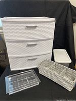 White Sterlite 3-drawer organizer, clear expanding drawer organizer, woven storage basket, and white plastic shoebox with lid arranged on black background.