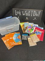 Photo showing the full lot contents including soft pastel sets, plastic storage container, children's coloring books, packets of wood hair clips and clothespins, and the hanging artwork display board.