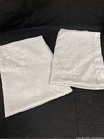 Two white sheer embroidered floral sheet panels folded on black background.