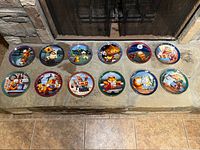 Twelve Garfield collector plates laid out in two rows on stone hearth, showing colorful Garfield themed illustrations on each plate.