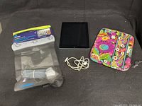Photo showing Apple iPad, white charging cable, Vera Bradley padded sleeve, and Aquapac waterproof case.