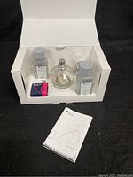 Starter kit items including glass lamp, two fragrance bottles, replacement wick, and instruction booklet in white display box