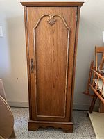 Front view of a wooden standing cabinet chest with a single door showing decorative floral carving and metal handle.