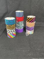 13 rolls of duct tape stacked in three columns showing various decorative colorful patterns. Some rolls are partially used and some appear new.