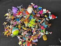 A large pile of plastic toy animals of various brands and series on a black background, showing many colorful small figures.