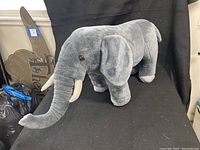 Side profile view of the large gray stuffed elephant showcasing the tusks, trunk, and overall shape against a black backdrop.
