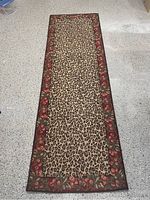 Full view of the rectangular carpet runner showing leopard print center and red floral border with floral design, placed on a grey floor.