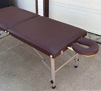 Brown vinyl upholstered massage table with aluminum folding legs and detachable U-shaped face cradle