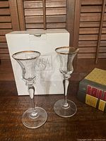 Pair of clear crystal candle holders with gold trim rims standing in front of the Mikasa box on a wooden surface.