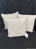 Three linen throw pillows with a looped diagonal embroidery design displayed against a black background.