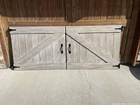 Pair of grey wash wood twin headboards lying flat side by side, showing entire barn door design with black metal corner hinges and pull handles.