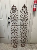 Pair of iron scrollwork wall hangings standing vertically against a door, showing full length and design details.
