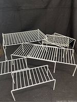 Six white coated wire shelf organizers of various sizes arranged for display, showing grid and striped wire designs