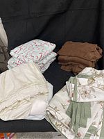 Photo showing folded bedding sets: candy cane flannel sheets, brown knit sheets, white eyelet dust ruffle, and floral duvet cover pieces.