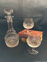 Full set of Waterford Colleen brandy snifters and Galway Crystal decanter with stopper shown on a black background with books behind.
