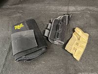 Photo showing a set of three braces: one Everlast black back support brace, one black right wrist brace, and one beige left wrist brace placed on a dark surface.