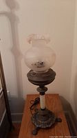 Full view of antique table lamp showing milk glass shade with floral designs and brass base with ornate lion paw feet.