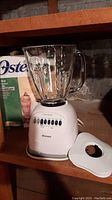 Oster blender assembled with glass jar and lid beside it on a shelf, showing overall look and size.