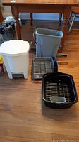 Full view of all items on floor including two garbage bins and two dish racks placed in front of a table.