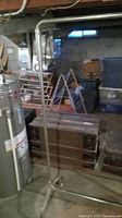 Standing metal garment rack in a basement or storage area surrounded by boxes and other stored items. Photo shows full rack frame, no clothes hung.