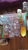 Top view of multiple clear glass candle holders, glassware, a white pitcher with lemon images, and a yellow plastic bowl on a wooden table