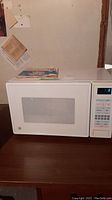 Front view of white GE microwave with control panel and door window visible, placed on dark wooden surface.