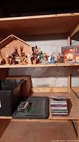 Wide view of wooden shelf with nativity figurines on upper shelf and stack of Christmas CDs on lower shelf