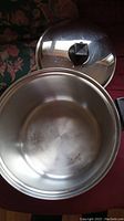 Large stainless steel roaster pot with lid, showing inside of the pot and lid with black knob handle.
