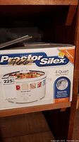 Front box view showing Proctor Silex 4 Quart slow cooker model 33140, including branding and dishwasher safe stoneware and lid label.