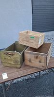 Four wooden storage containers displayed together on a table outdoors, showing size and condition.