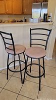 Two metal bar stools with black metal frames and light cloth seats positioned on tile floor in kitchen area.