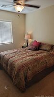 Wide view of the queen size bed made with Asian inspired bedding in red and gold tones, showing the bed frame, bedding, and bedside lamp.