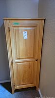 Front view of a tall wooden cabinet with closed door and single brass knob.