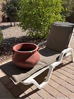Chaise lounge with cushion outside on paver patio with clay pot placed on it, showing overall size and condition.