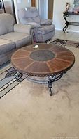 Wide shot showing the round wood grain coffee table in front of couches with metal base and faux studded side design.