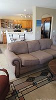 Brown cloth couch with subtle pattern and nailhead trim on arms, viewed from front and side in living room setting.
