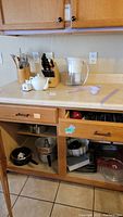 Photo of countertop showing wood block cutlery set with knives, white teapot, Brita water pitcher, and container with kitchen utensils.