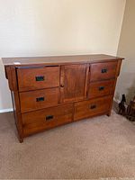 Front view of a medium brown wood dresser with six drawers and a central cabinet door showing the hardware and wood grain.