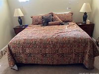 King size bed with southwest patterned bedding and pillows, two bedside tables with lamps, bed positioned against beige wall.