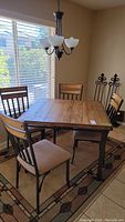 Kitchen table and four chairs set placed on a patterned rug near window, showing full view of table and chairs.