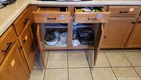 Open cabinet under kitchen counter showing glass baking dishes, mixing bowls, ramekins, and other kitchen items stored inside