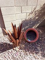 Metal agave yard art sculpture and clay sideways pot sitting on gravel in front of a cinder block wall.
