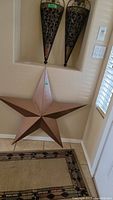 Photo of two metal sconces mounted on wall above a large metal star decor piece and rug runner beneath.