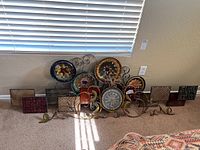 Multiple metal wall decorations arranged on floor; include circular floral medallions and square geometric pieces, rustic finish.