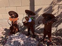 Full view of three rusted metal yard art musicians against cinderblock wall