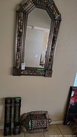 Front view of the metal/tin ornate mirror hanging on the wall with two candle holders below it.